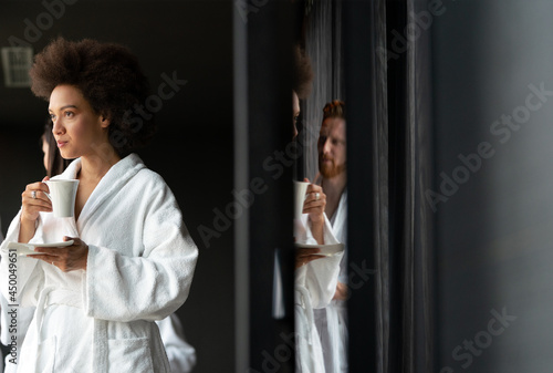 Beautiful black woman relaxing at luxury hotel spa wearing bathrobe and drinking coffee