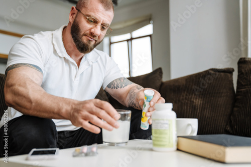 White bearded man taking his medicine while siting on couch at home