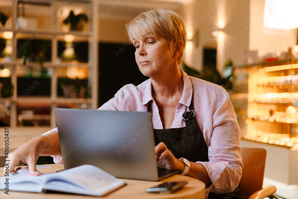 White mature woman working with laptop while sitting at table in cafe White mature woman working with laptop while sitting at table in cafe