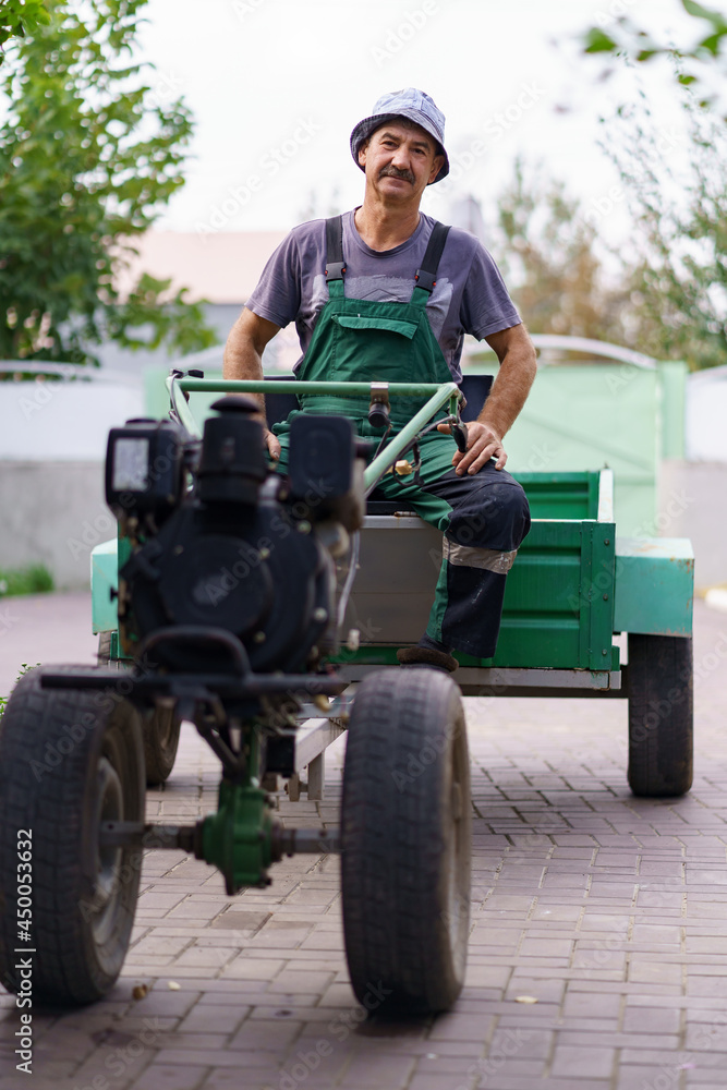 Satisfied farmer portrait sitting behind the wheel of a two-wheeled tractor.