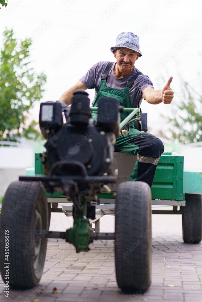 Fototapeta premium Satisfied farmer portrait sitting behind the wheel of a two-wheeled tractor.