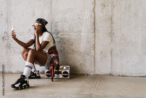 Black young woman using mobile phone while sitting on tape recorder