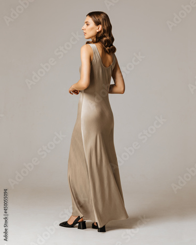 Studio photoshoot of a smiling young brunette woman wearing casual clothing against a brown background.  Natural makeup and wavy hairstyle
