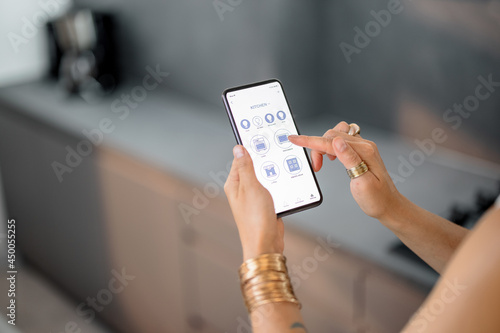 Smart phone with running mobile application to control smart devices in the kitchen. Female controlling smart devices with phone at home. Smart home concept