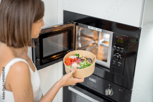 Woman heating food with microwave machine at home, female using modern kitchen appliances photo