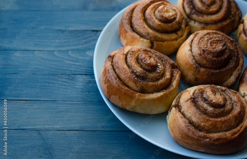 Homemade swirled rosy buns on a blue plate on the right on a blue wooden background Homemade swirled rosy buns on a blue plate on the right on a blue wooden background