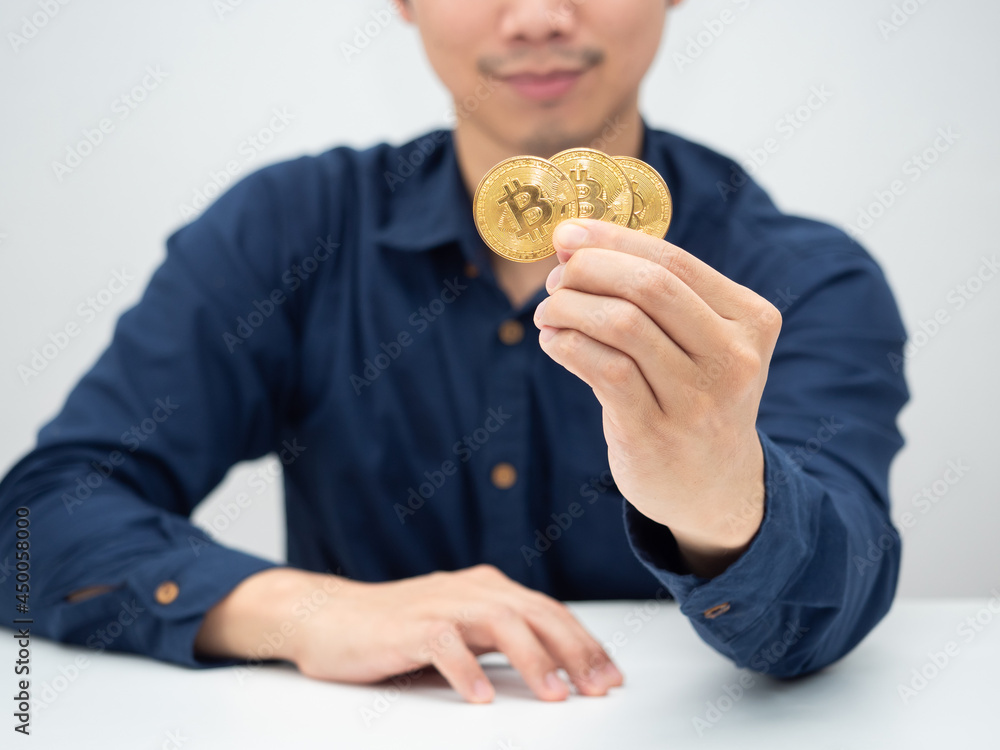 Man sitting at the desk and showing goldden bitcoin in his hand Man sitting at the desk and showing goldden bitcoin in his hand