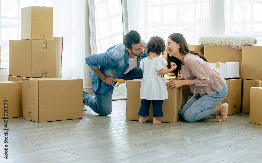 Caucasian handsome father, asian beautiful mother, little mixed race adorable girl or daughter sitting on floor, family playing together with happiness, moving house or apartment with paper boxes. Caucasian handsome father, asian beautiful mother, little mixed race adorable girl or daughter sitting on floor, family playing together with happiness, moving house or apartment with paper boxes.