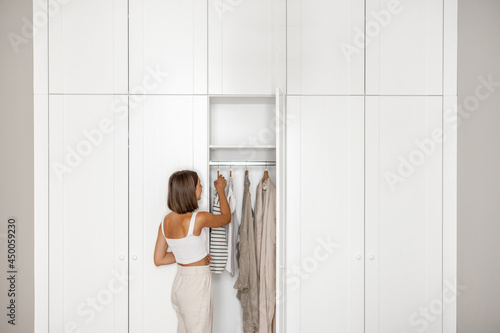 Young woman chooses what to wear, standing near the white closet at home. Concept of choice problem, style and fashion photo