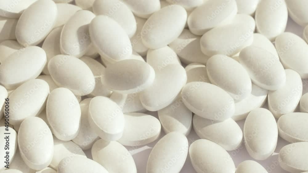 Production of new white vitamin tablets at the factory. White pills fall on a spinning platform with the same medications. All this is in the rays of bright light and contrasting shadows. slow motion Production of new white vitamin tablets at the factory. White pills fall on a spinning platform with the same medications. All this is in the rays of bright light and contrasting shadows. slow motion