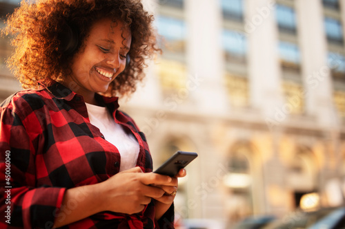 Young woman listening the music while walking through the city. Happy African woman with curly hair outdoors.