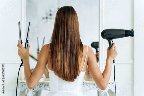 фотографія Back view of the pretty young woman posing for the camera with a hair dryer and