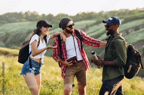 Group of friends, young men and woman walking, strolling together in summer forest, meadow. Active lifestyle, friendship, travel concept