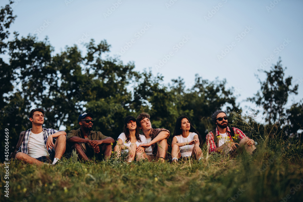 Obraz premium Meet sunset. Group of friends, young men and women walking, strolling together in summer forest, meadow outdoors. Active lifestyle, friendship