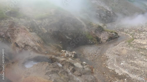 The water is bubbling and splashing in the boiler of the geyser. Hot steam is flying over the ground. The river flows along a rocky bed. Sulfur deposits around. Kamchatka. Valley of Geysers