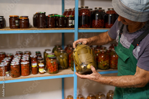 Man satisfied with the result of his work. He watches the shelves with marinated veggies in glass jares. Fermented organic food. photo
