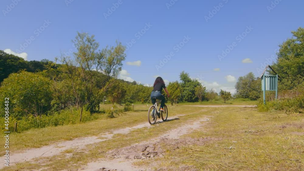 View from the back of a girl riding a bike on the road. Cycling on a field road. Young woman pedals a bicycle View from the back of a girl riding a bike on the road. Cycling on a field road. Young woman pedals a bicycle