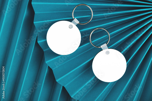 Top view of two keychain mockup with empty round pendants placed on blue paper fans. Key chain mock up photo