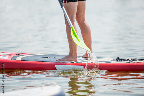 Male legs stand up sup paddleboarding on ocean blue water background. Summer vacation leisure	