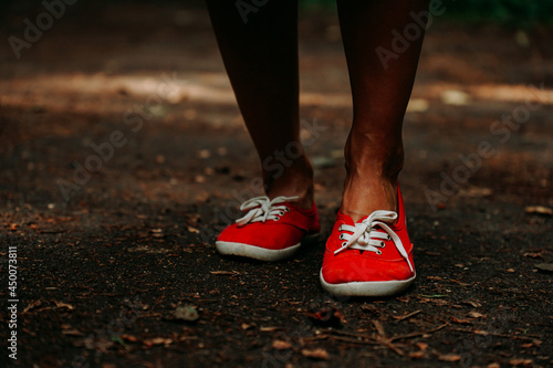 Legs in red sneakers on an autumn path in the park. Black leather legs. Sport in summer forest