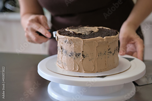 Woman pastry chef making chocolate cake with chocolate cream, close-up. Cake making process, Selective focus