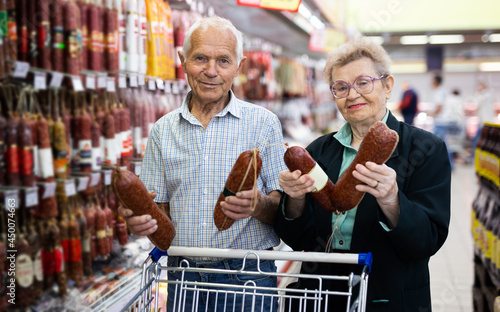 mature couple chooses out salami in meat section of supermarket