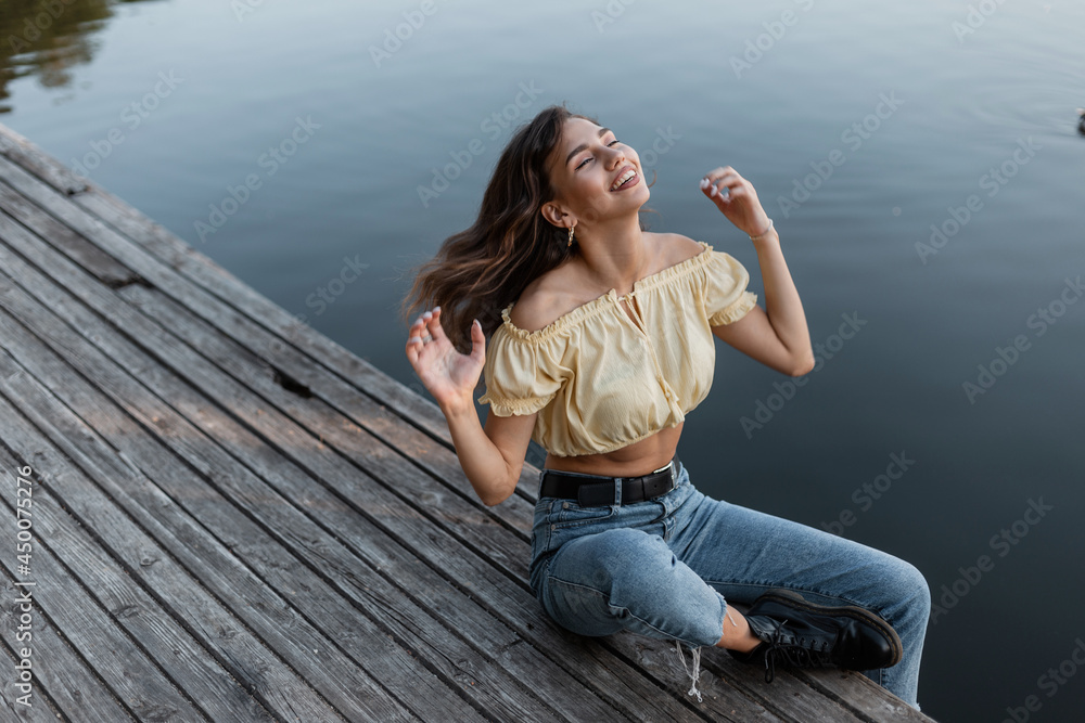 Beautiful happiness woman with blue jeans, yellow fashion top and boots enjoying outdoor and recreation by the lake on wooden pier. T Beautiful happiness woman with blue jeans, yellow fashion top and boots enjoying outdoor and recreation by the lake on wooden pier. T