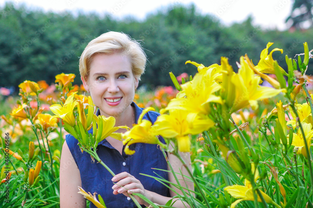 Blue-eyed blonde woman among lushly blooming yellow lilies in the garden Blue-eyed blonde woman among lushly blooming yellow lilies in the garden