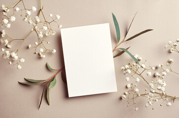 Wedding invitation card mockup with natural eucalyptus and white gypsophila twigs. Blank card mockup on beige background.