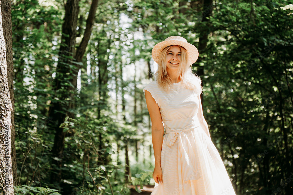 Beautiful young woman in a straw hat and white dress in a green park or forest on a summer day