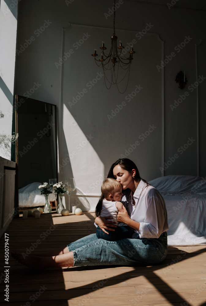Fototapeta premium happy brunette mom and baby girl kissing on the wooden floor in the rays of light