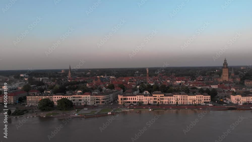 Aerial approach above extreme high water levels of river IJssel showing countenance boulevard of Dutch Hanseatic tower town Zutphen in The Netherlands at sunset. Climate and weather condition concept. Aerial approach above extreme high water levels of river IJssel showing countenance boulevard of Dutch Hanseatic tower town Zutphen in The Netherlands at sunset. Climate and weather condition concept.