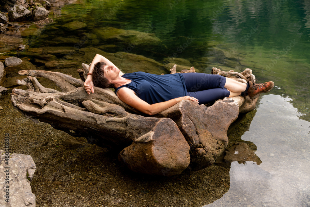 große Holzwurzel im Alpensee, Frau liegt in der Wurzel und genießt Ruhe und Stille der Natur.