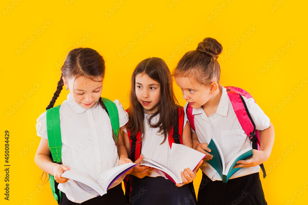 The little schoolgirls are reading the books at the yellow background The little schoolgirls are reading the books at the yellow background