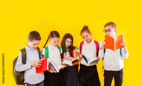 Happy excited smiling little students holding color books isolated on yellow background. Back to school.