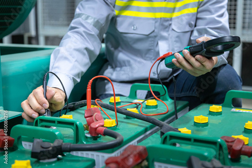 Close up hand engineer working on checking and maintenance with batteries for diesel generator unit has a unit mounted radiator and fuel filter system at emergency power supply room. photo