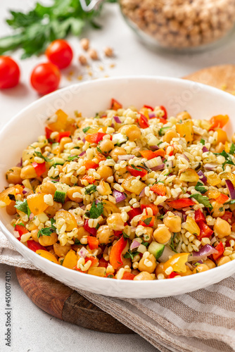 Salad of bulgur, chickpeas and vegetables in a bowl close-up. Salad with chickpea, bulgur, tomato, pepper, cucumber, onion, parsley, and lemon juice. Vegan food, Middle Eastern food.