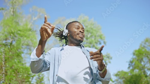Happy black man dancing to music in earpads in green park, outdoors relax photo
