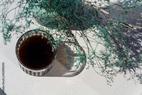 Faceted glass with black filter coffee on arabika beans in third-wave coffee shop, on the background of white table with blue flowers.