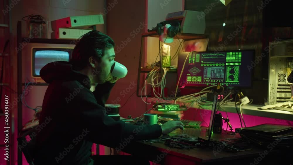 Young hacker typing on keyboard at night, breaking password, using laptop and drinking coffee at night. Man developing program in dark room. Programmer infecting system with cyber virus Young hacker typing on keyboard at night, breaking password, using laptop and drinking coffee at night. Man developing program in dark room. Programmer infecting system with cyber virus