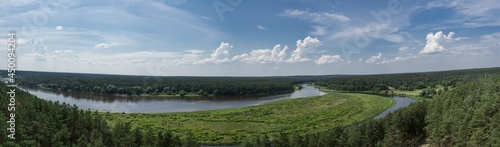 Panoramic view from the top of Merkine observation tower onto Nemunas river and surrounding riverbanks covered with green forest. Warm summer day. White clouds in blue sky.