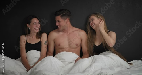 Handsome young man and two beautiful women in bed. Polyamory concept