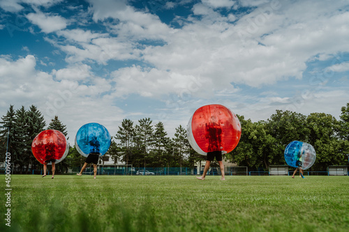 People playing in Bubble Football. Zorbing bumper football soccer on a green field © Jan