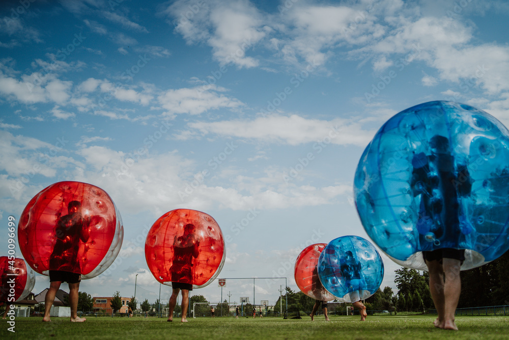 Obraz premium People playing in Bubble Football. Zorbing bumper football soccer on a green field