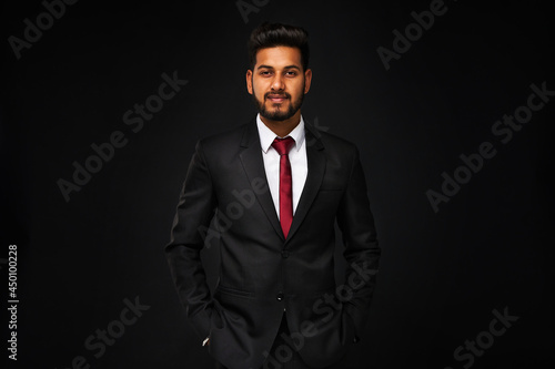 Portrait of young indian business man in black suit on black isolated background