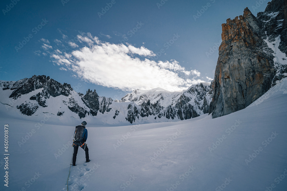 An alpinist on a glacier walking towards big alpine mountain. Climber on a alpine ascent in Mont Blanc massif near Chamonix, France. High alpine landscape and mountaineer on the climb towards summit.