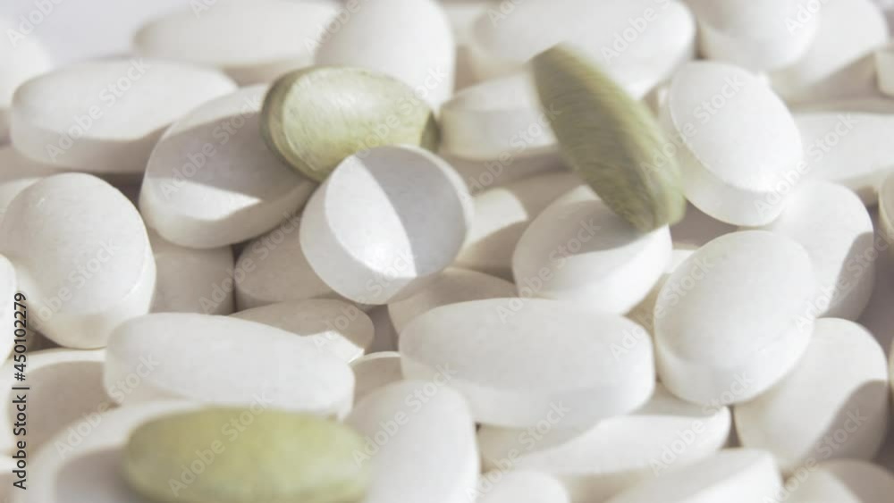 Pharmaceutical production new green pills fall on ordinary white pills that rotate on a white platform. Production of cannabis tablets, herbal tablets, pharmaceutical industry. Slow motion. Close up. Pharmaceutical production new green pills fall on ordinary white pills that rotate on a white platform. Production of cannabis tablets, herbal tablets, pharmaceutical industry. Slow motion. Close up.