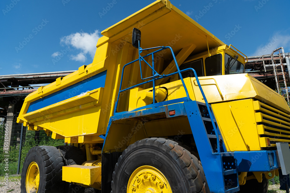Heavy yellow dump truck for transporting iron ore and coking coal at a metallurgical plant on a bright sunny day Heavy yellow dump truck for transporting iron ore and coking coal at a metallurgical plant on a bright sunny day