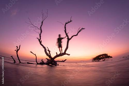 Stunning sunset sky above the Gili Trawangan Island, Lombok . silhouette of a person on a tree waves and colorful clouds. Long exposure photo