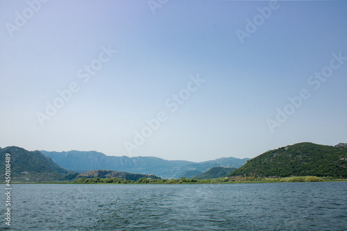 Landscape with lake and green mountains against the background of a clear sky. Panoramic beautiful view on largest lake. Wonderful summer day.